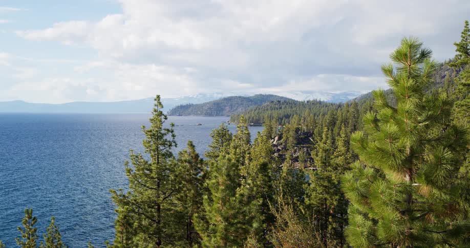 A lake with trees on the shoreline with a mountain range the sky and clouds in the background