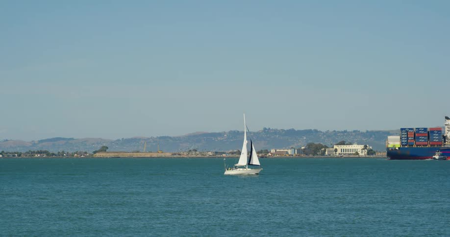 Sailboat and cargo freighter pass town loomed over by low mountain