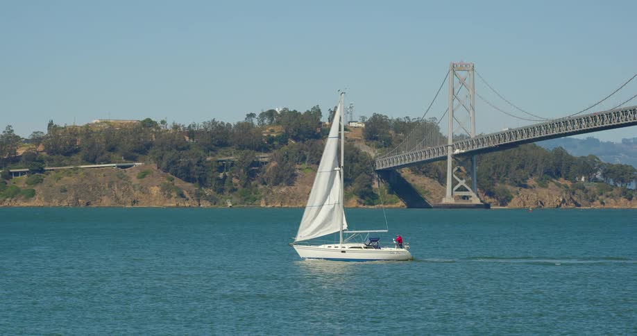 A person relaxes on the back of a sailboat as it travels across a waterway on a sunny day