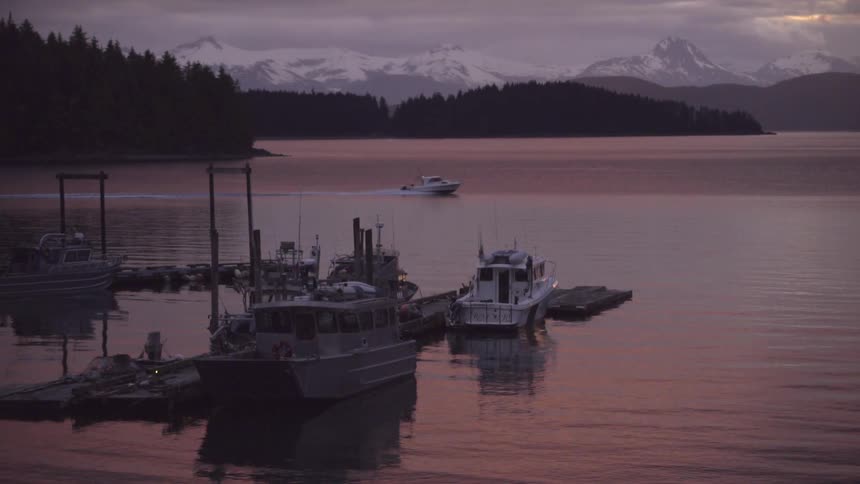 A boat moves across a lake at sunrise with a boat dock and snow covered mountains