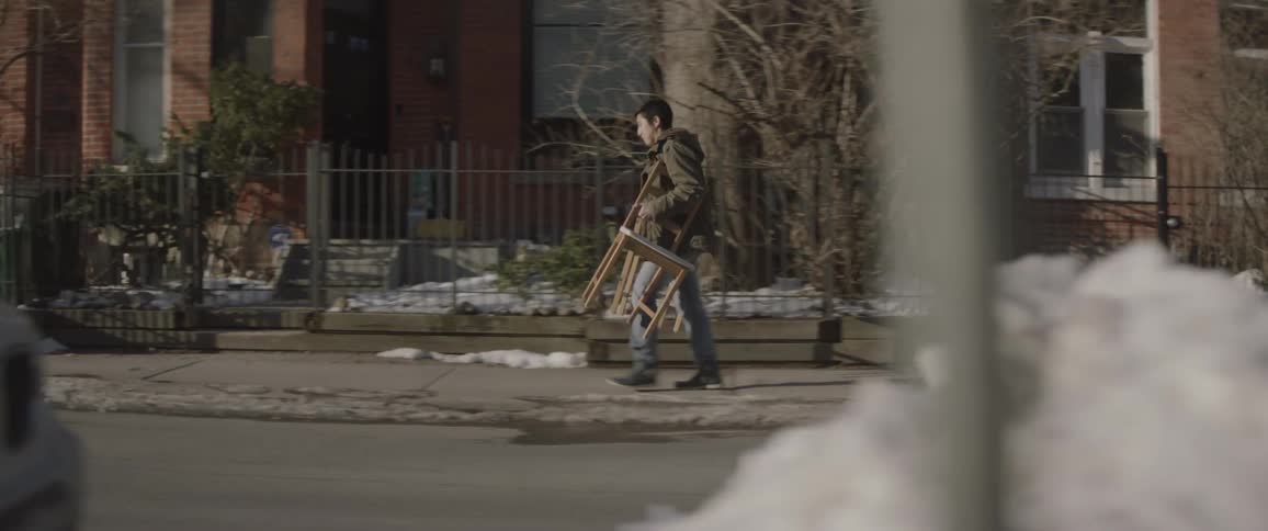 A man carries chairs down a sidewalk