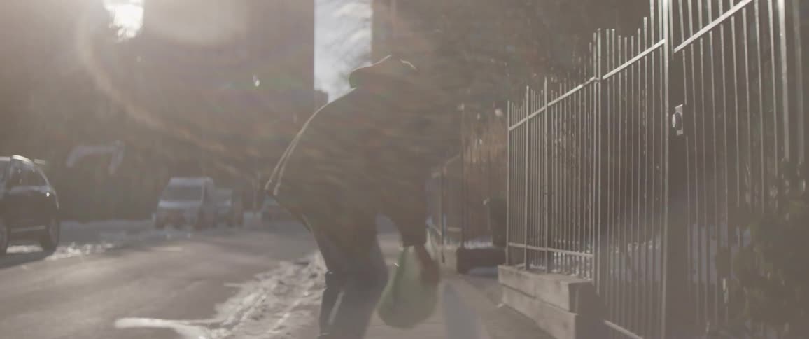 A man is carrying groceries down a city street as one bag breaks