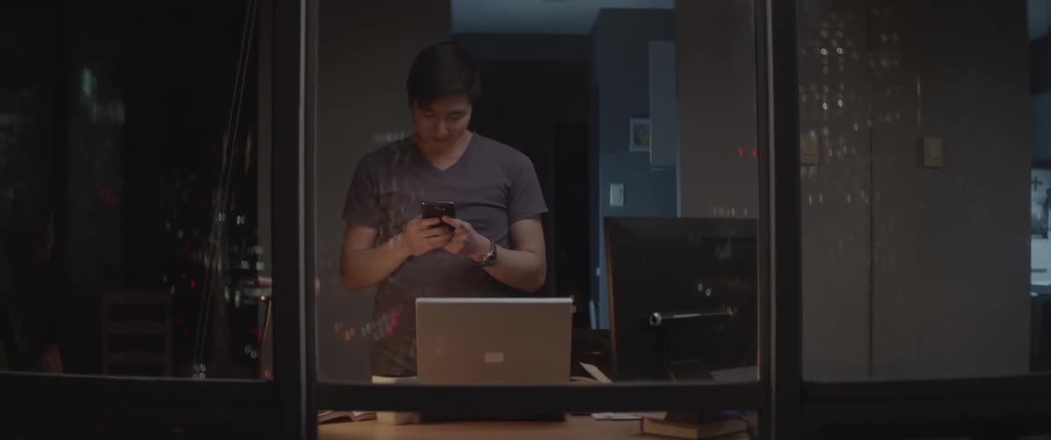 A man uses his phone standing by a window
