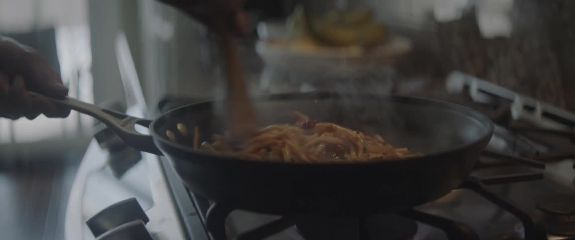 A man stirs noodles in a skillet