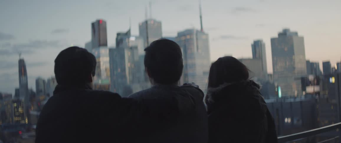 Three people are by a balcony looking at the view of a city