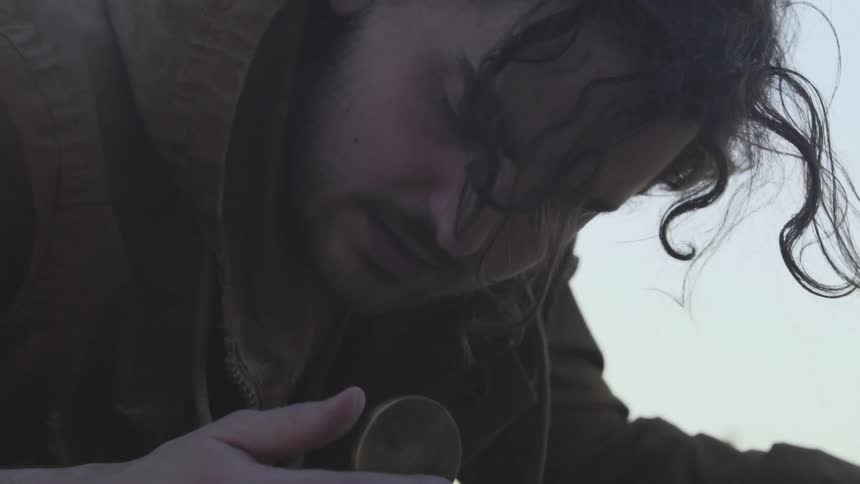 A man looks at a compass while laying face down on the ground