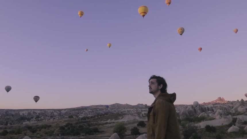 A man looks around at multiple hot air balloons flying all over