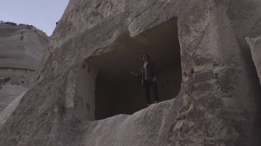 A man stands at the edge of a cave opening