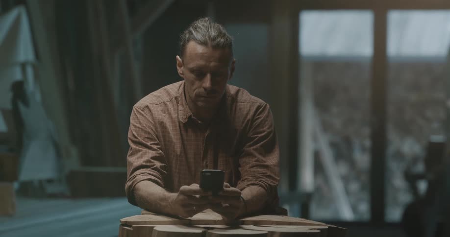 A man leaning on a slab of wood texts on his cell phone