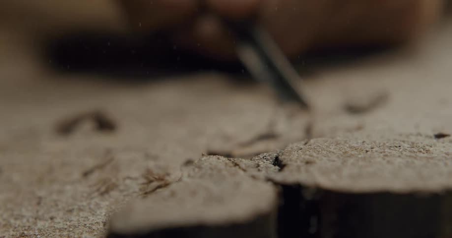 A person chisels away at a piece of wood covered in sawdust
