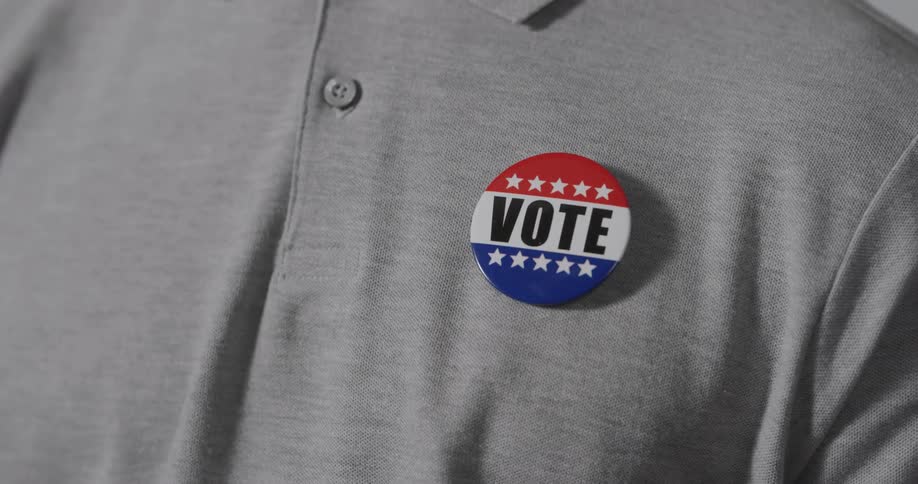 A man pins a vote button to his gray polo shirt
