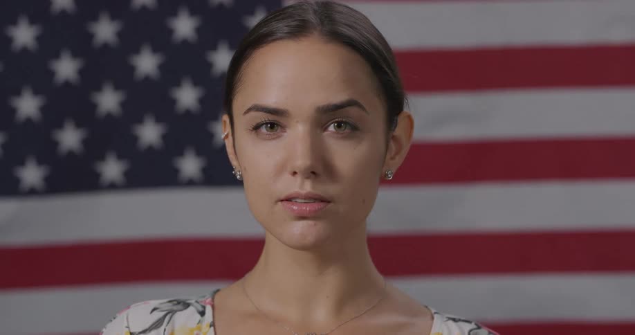 A woman standing and staring with an american flag waving in the background