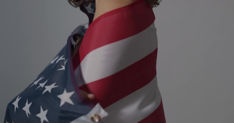 A woman wraps an american flag around her shoulders as the flag and her hair flap in a gentle wind