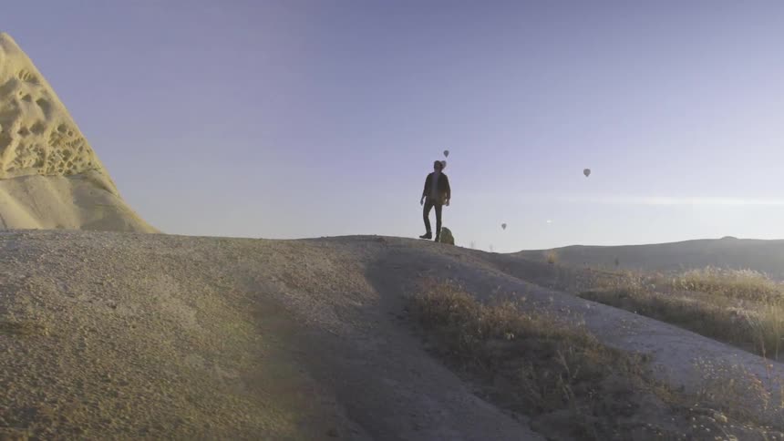 A man is standing on a hill looking around at the sky