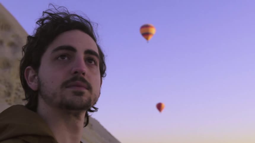 A man with brown hair looks up at hot air balloons