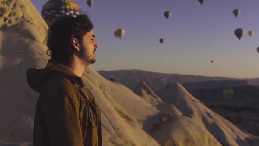 A man looks around at a sky filled with hot air balloons