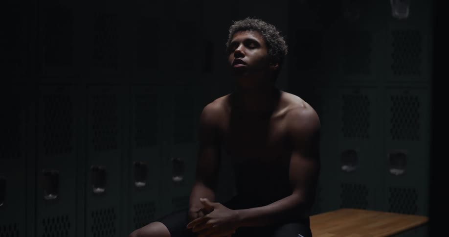Young muscular man sitting in a dimly lit locker room talks to himself nervously