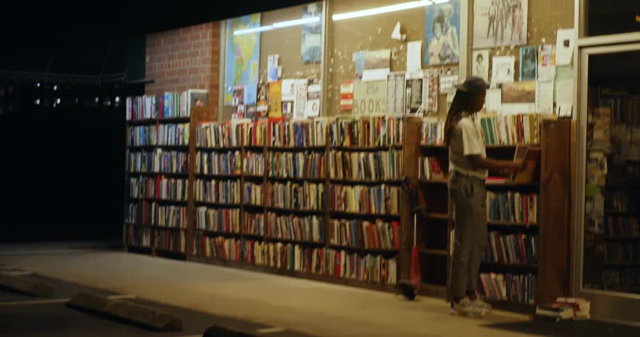 A young male stands outside of a bookstore and browses through the contents of outdoor bookshelves