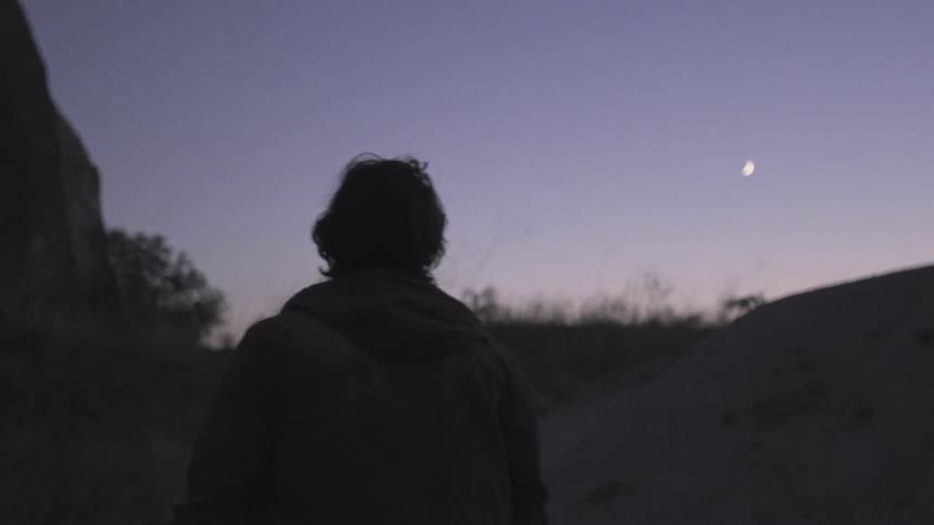 A man walks over hilly terrain at night