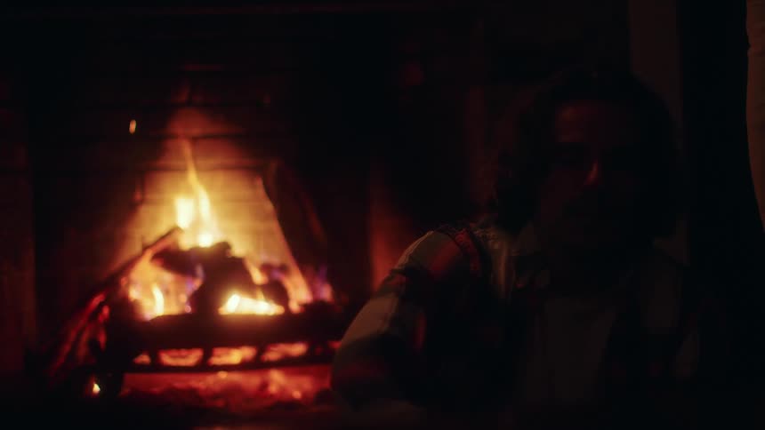 A man sitting in front of a burning fireplace in his dark house