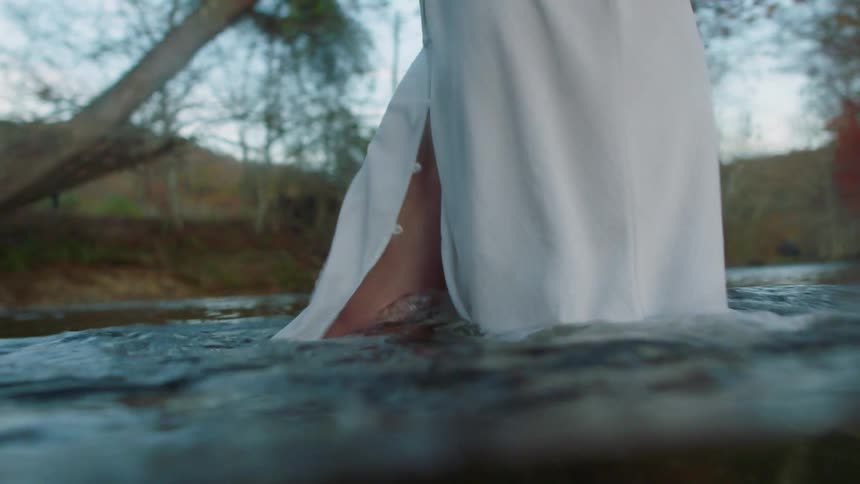 A barefoot woman walks across a river towards a person waiting on the other side