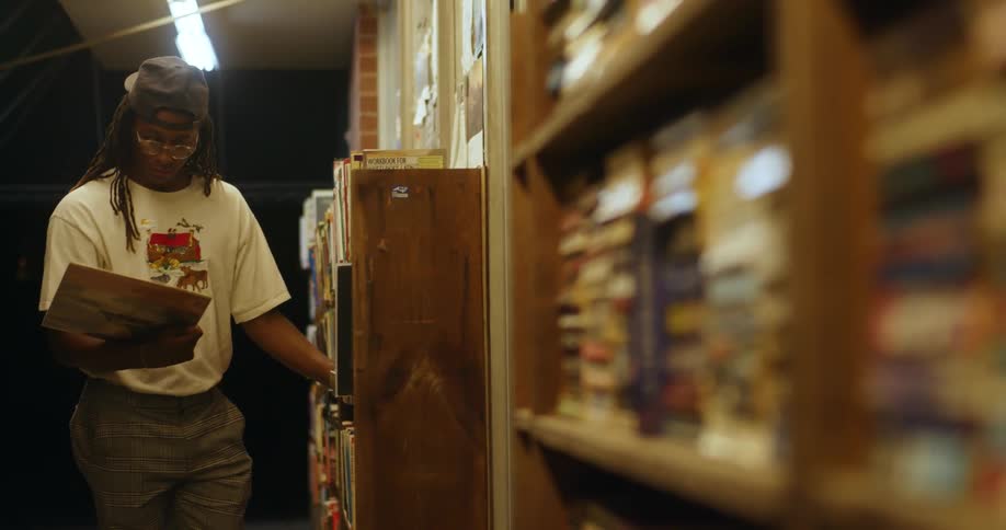 A man with a hat and glasses taking a record from a shelf