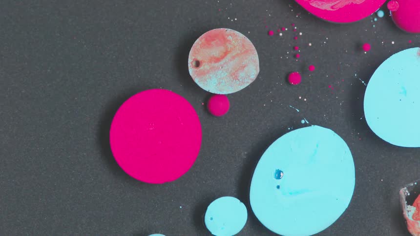 Spots of pink and aqua paint float atop the surface of a clear liquid