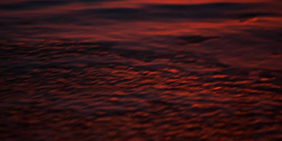 The water moves fast under the red sky