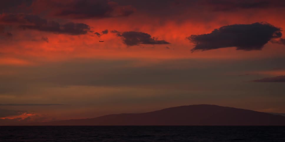 Clouds floating in a red sky above a hill landscape at dusk