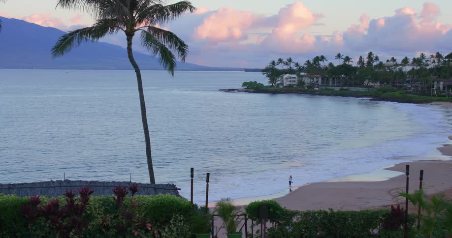 A lone person walking on a sandy tropical beach at sunset