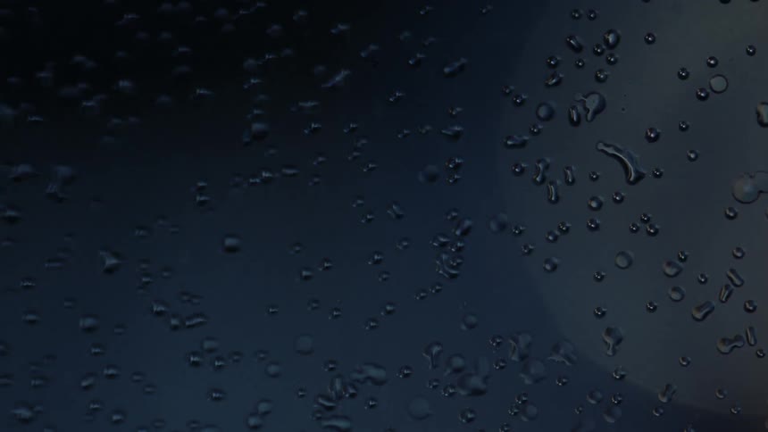 A light shines behind a water covered glass surface