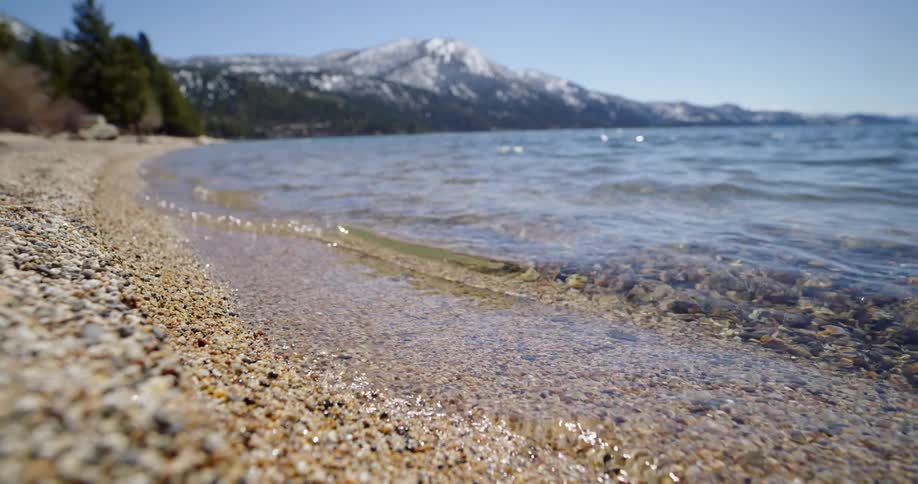 Lake water flowing onto a sandy shoreline with a snowy mountain in the distance