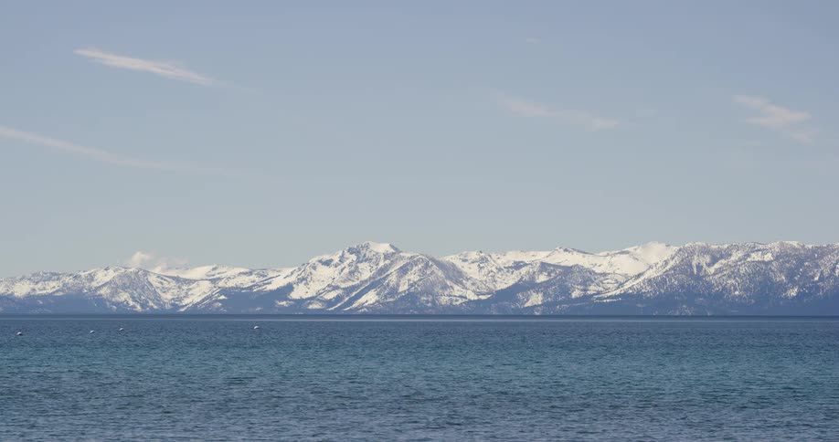 The ocean sits next to the snow covered mountains under a blue sky