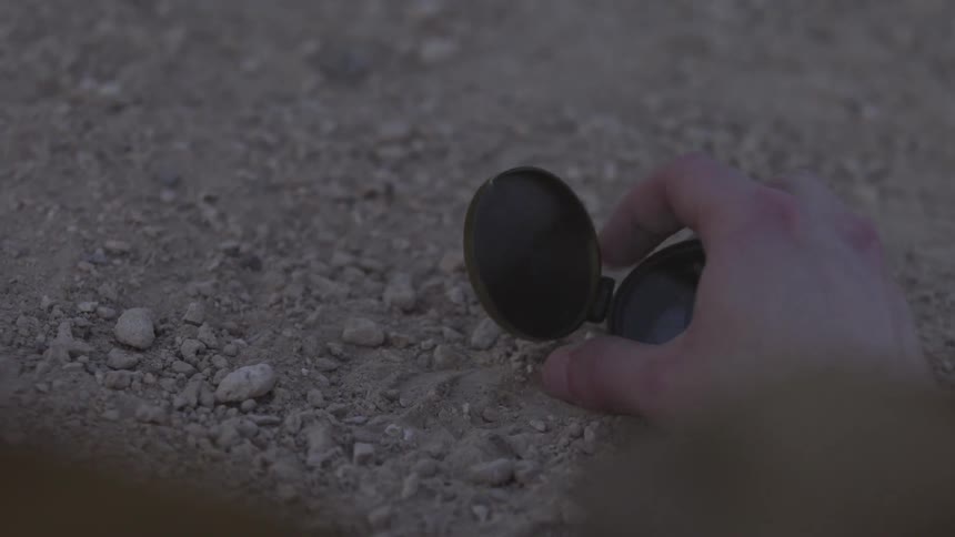 A person examines a compass on the ground