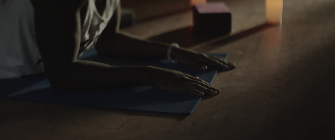 A man on a yoga mat holds a stretch in a candle lit room