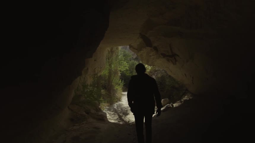 A person is walking out of a dark cave