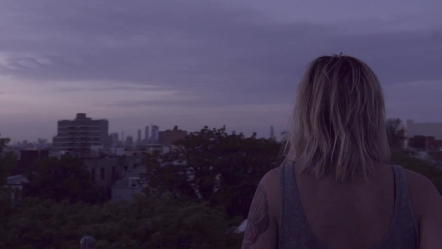 A woman stands outside looking at a town below