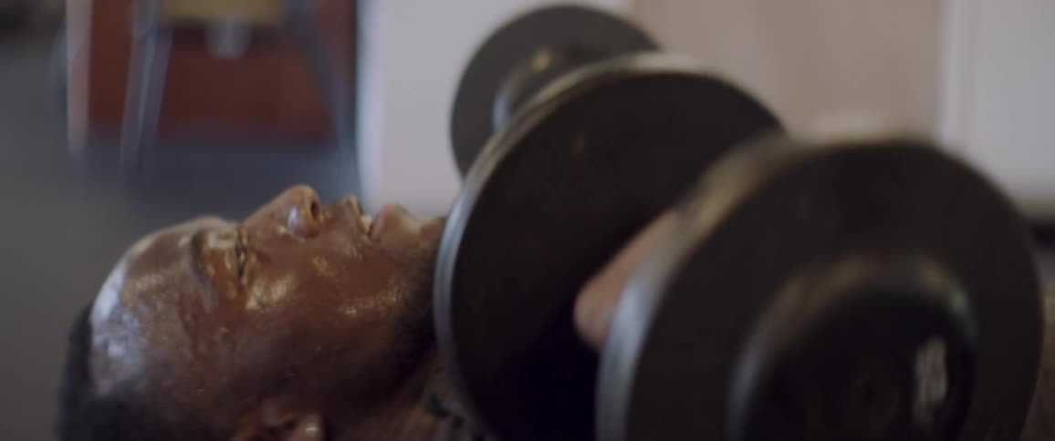 Sweaty man lifts weights while laying down