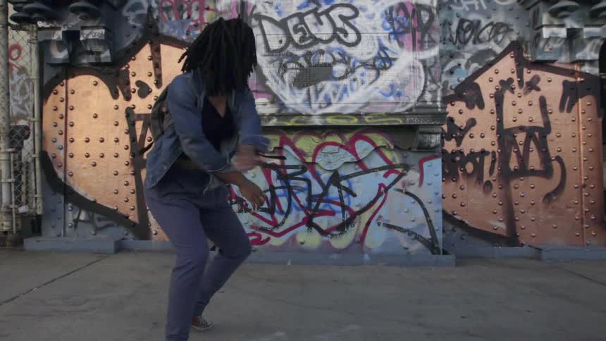 A woman dances in front of a wall of graffiti