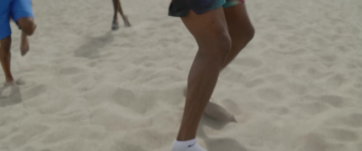 Male athletes are practicing footwork drills in the sand at the beach