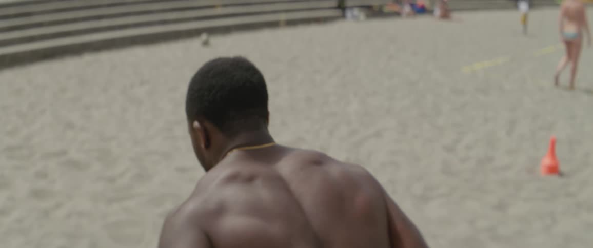 A shirtless man hops on a sandy beach