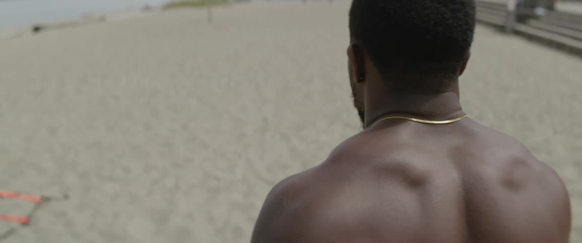 A shirtless man walks on a sandy beach