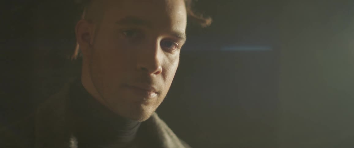 Man looking into the camera as lights come and go on his face in a dark scene