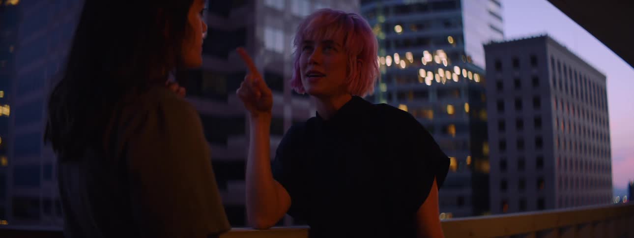 A pair of women chat and laugh while relaxing on the balcony of a building in a metropolis at night
