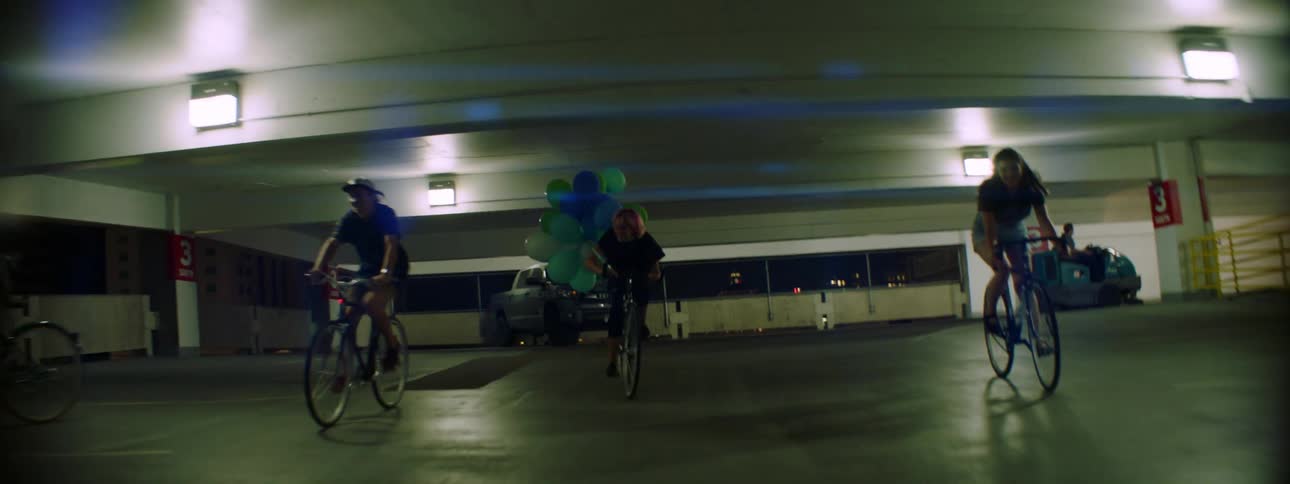 A group of young women ride bicycles together through a multi story parking garage