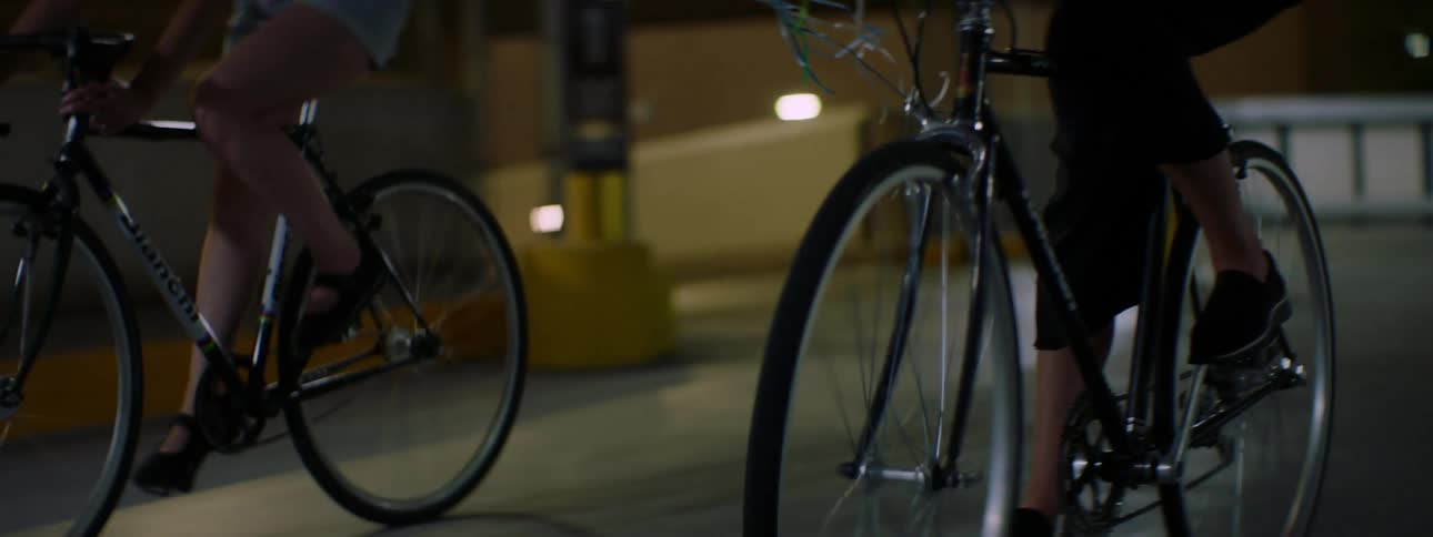 A teenager rides a bicycle holding balloons inside a public vehicle garage