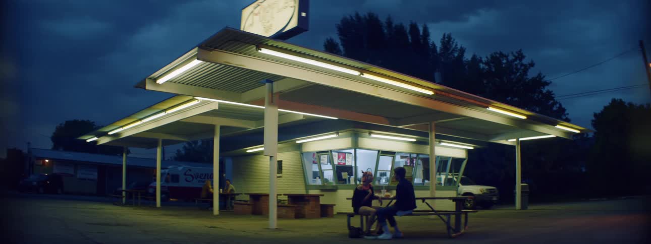 Young couple sitting in a diner outdoors kiss and laughs while eating burgers on a summer afternoon