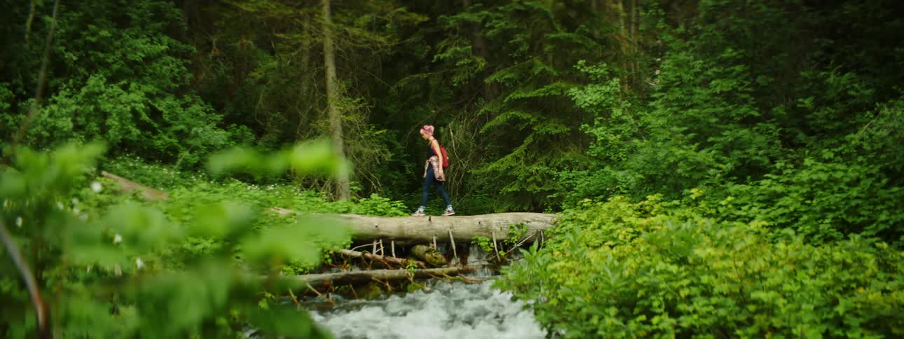 A woman hikes over the stream