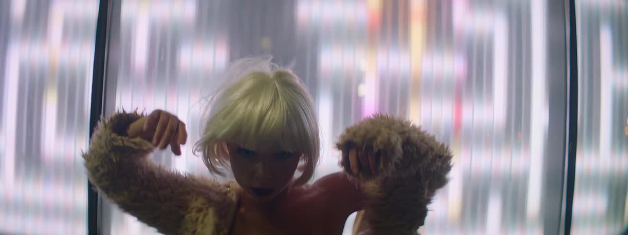 Young woman wearing white wig dances in front of an electronic display on the street at night