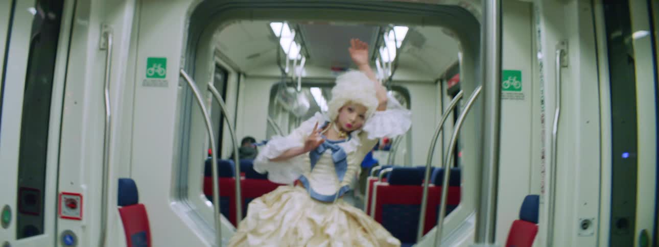 Woman in a victorian costume dances inside the car of a train moving through the city at night